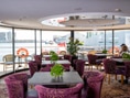 Restaurant mit lila Sesseln, Tischen und grossen Fenstern mit Blick auf das Wasser.