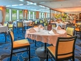 Elegantes Restaurant mit gedeckten Tischen, blauem Teppich und grossen Fenstern.