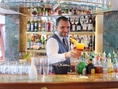 Barkeeper reicht Getränk an gut ausgestatteter Bar.
