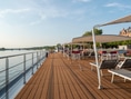 Deck eines Kreuzfahrtschiffs mit Liegestühlen und Sonnensegeln am Flussufer.