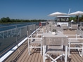 Sonnendeck eines Schiffes mit Tischen und Stühlen am Fluss.
