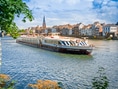 Grosses Flussschiff auf einem Fluss mit Stadt im Hintergrund.
