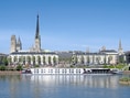 Flusskreuzfahrtschiff vor Stadtsilhouette mit Kirchen.
