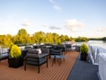 Terrasse eines Schiffs mit Sitzmöbeln auf einem Fluss, umgeben von Bäumen.