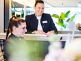Zwei lächelnde Frauen in Büro-Outfit an einem Tresen.