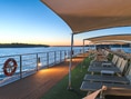 Deck eines Flusskreuzfahrtschiffs bei Sonnenaufgang, mit Liegestühlen und Wasserblick.