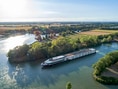 Flusskreuzfahrtschiff fährt auf einem Fluss durch eine ländliche Landschaft.