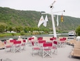 Deck eines Flusskreuzfahrtschiffs mit leeren Stühlen und Flusslandschaft.