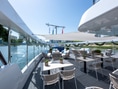 Sonnige Terrasse eines Bootes mit Tischen und Stühlen am Fluss.