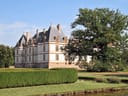 Schloss neben einem grossen Baum und Hecken, umgeben von einem Wassergraben.