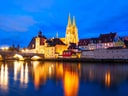 Abendansicht der beleuchteten Stadt mit Kirche und Flussreflektion.