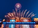 Feuerwerk über Bühne auf schwimmender Plattform bei Nacht.