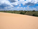 Sanddüne vor grüner Hügellandschaft und blauem Himmel mit Wolken.
