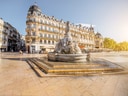 Historische Gebäude und Brunnen auf sonnigem Platz.