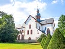 Eine weisse Kirche mit Turm, umgeben von gepflegtem Garten und blauem Himmel.