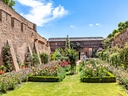 Blühender Garten vor einer historischen Steinmauer unter blauem Himmel.