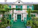 Pinkes Haus mit grünen Fensterläden und überwuchertem Garten.
