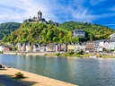 Schloss auf Hügel über Fluss und bunte Häuserreihe.