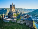Burg auf einem Hügel umgeben von grünen Hügeln und einem Fluss.