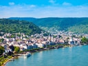Luftaufnahme einer Stadt am Fluss mit Hügeln im Hintergrund.