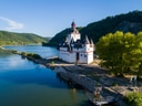 Schloss auf einer Insel im Fluss, umgeben von Bäumen und Hügeln.