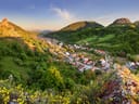Panoramablick auf ein Dorf in einem grünen Tal mit Hügeln und Felsen.