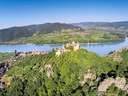 Luftaufnahme einer Flusslandschaft mit Burg und Bergen im Hintergrund.