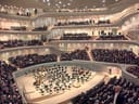 Volles Konzertsaal mit Publikum und einer leeren Bühne.