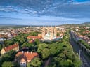 Luftaufnahme einer Stadt mit Dom und bewaldeten Hügeln.