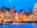 Weihnachtsbaum und Statuen auf beleuchtetem Platz bei Dämmerung.