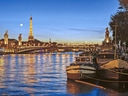 Eiffelturm bei Nacht mit beleuchteter Brücke und Booten auf der Seine.