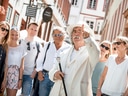 Mann im weissen Anzug führt Touristengruppe durch Altstadt.