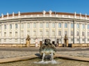 Blick auf ein grosses historisches Gebäude mit Brunnen im Vordergrund.