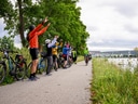 Gruppe von Radfahrern begrüsst Radfahrer auf Flusspfad.