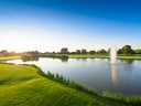 Grüner Golfplatz mit Teich und Springbrunnen bei Sonnenuntergang.