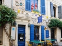 Aussenansicht eines Cafés mit blauen Fenstern und Stühlen.
