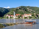 Flusslandschaft mit Stadt, Hügeln und Boot im Vordergrund.