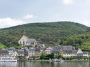 Hügelige Landschaft mit Dorf, Kirche und Burgruine am Fluss.