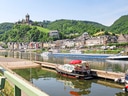 Fluss mit Booten und Hügel mit Burg im Hintergrund.
