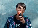 Person mit Brille isst Eis in schwarzer Waffel vor blauer Wand.