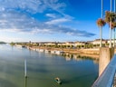 Flussufer mit Boot und Brücke unter blauem Himmel.