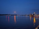 Abendlicher Hafenblick mit beleuchteter Brücke und Mond.