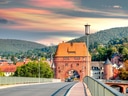 Brücke führt zu historischem Torbau, bewaldete Hügel im Hintergrund.