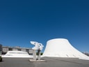 Weisses architektonisches Gebäude mit Skulptur davor und blauem Himmel.