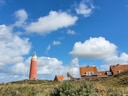Roter Leuchtturm und Häuser unter blauem Himmel mit Wolken.
