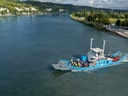 Blaues Fährschiff auf einem Fluss mit grüner Landschaft.
