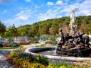 Springbrunnen in einem blühenden Park mit Hügeln im Hintergrund.