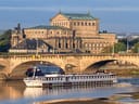 Boot auf dem Fluss vor einer historischen Brücke und einem grossen Gebäude im Hintergrund.