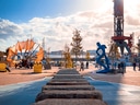 Hafenplatz mit blauer Statue und oranger Struktur im Sonnenschein.