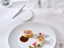 Elegantes Gericht auf weissem Teller, dekorativ angerichtet, mit Besteck und Blumendekoration auf weisser Tischdecke.